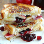 A decadent grilled cheese sandwich with brie and cranberries, styled alongside fresh apples and rosemary sprigs.