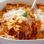 A spoon lifting a portion of creamy bow tie pasta lasagna, with stretchy melted cheese.