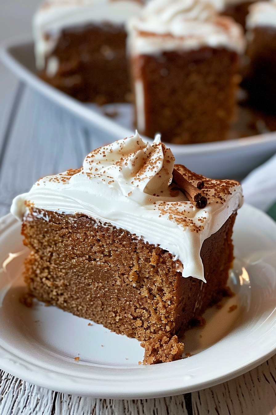 A slice of moist gingerbread cake topped with whipped cream and a dusting of cinnamon on a white plate.