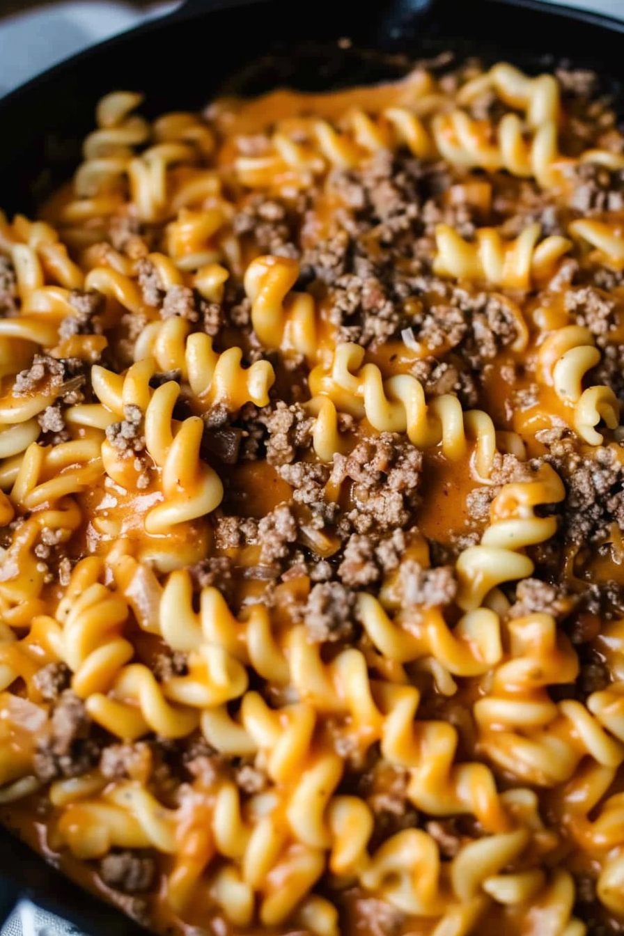 Close-up of cheesy pasta spirals with a savory ground beef sauce in a skillet.