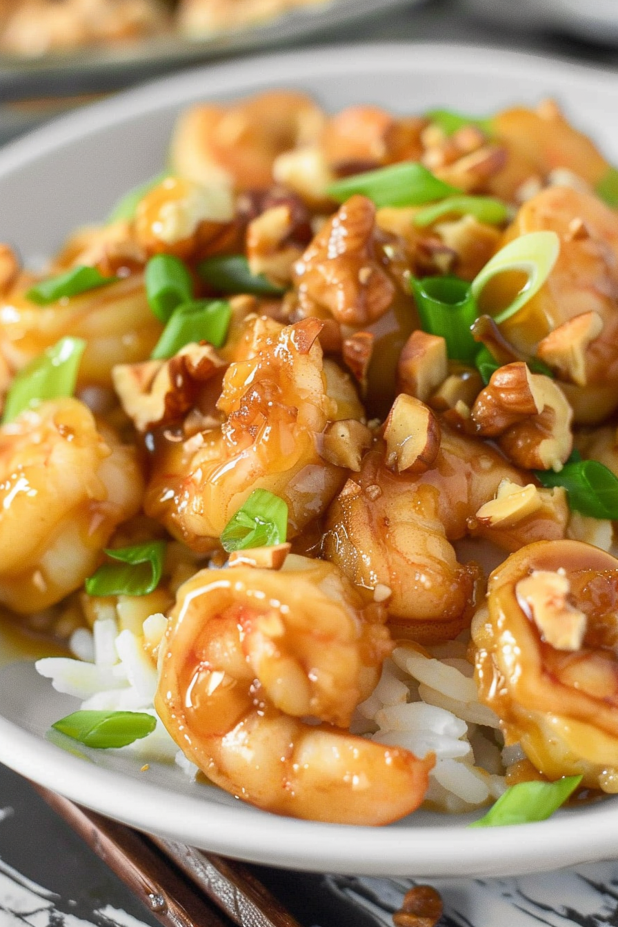 Close-up of golden honey-glazed shrimp garnished with crunchy walnuts and fresh green onions, served over fluffy white rice.