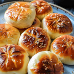 A stack of freshly cooked pan-fried buns garnished with sesame seeds, sitting on a rustic blue plate.