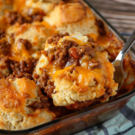 A spoon lifting a serving of cheesy Sloppy Joe casserole with perfectly browned biscuits.