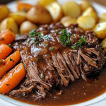 Slow Cooker Pot Roast with shredded beef, baby potatoes, glazed carrots, and rich brown gravy garnished with fresh herbs on a white plate.