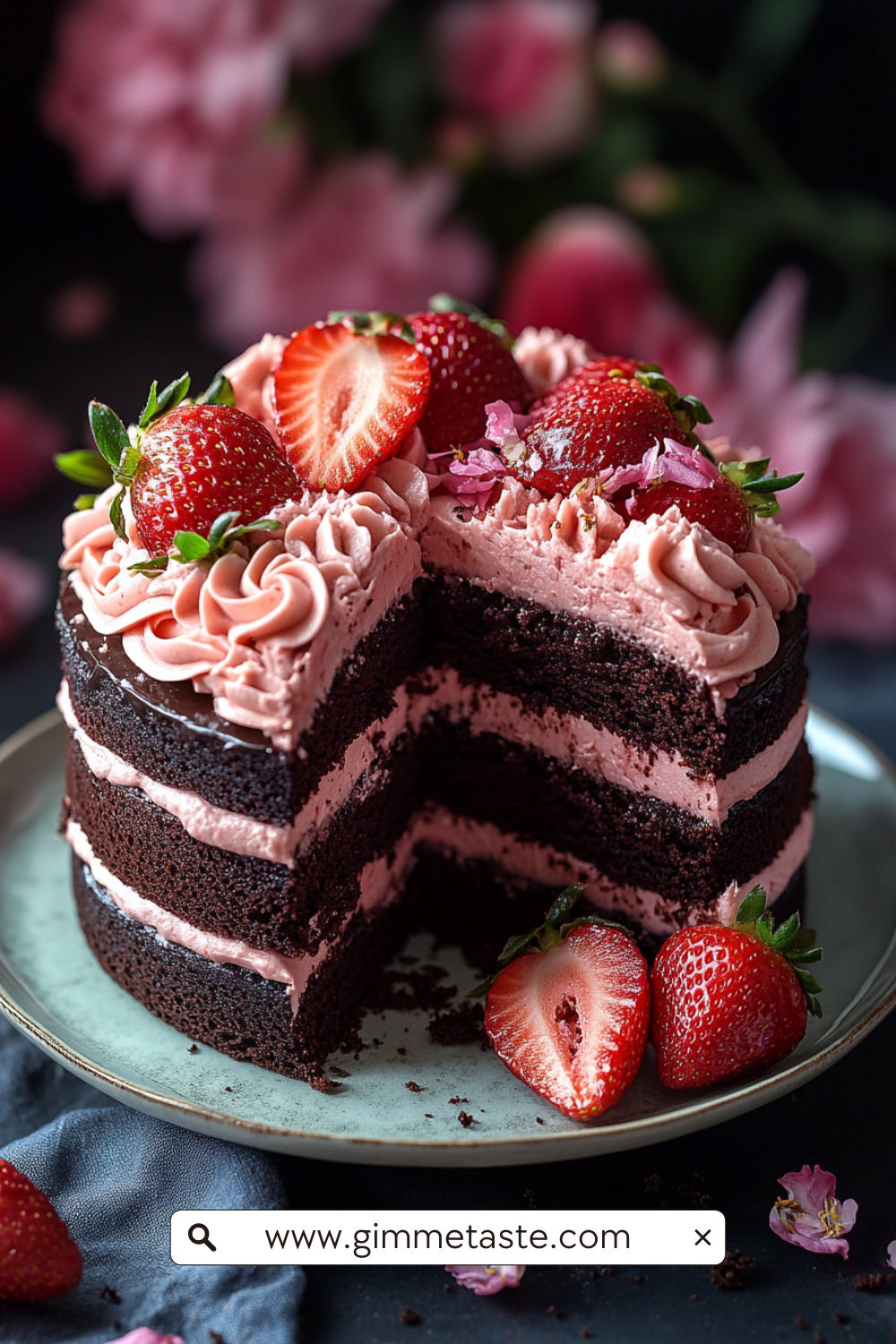 A decadent chocolate layer cake filled and topped with pink strawberry frosting, adorned with whole and halved fresh strawberries and edible flowers.