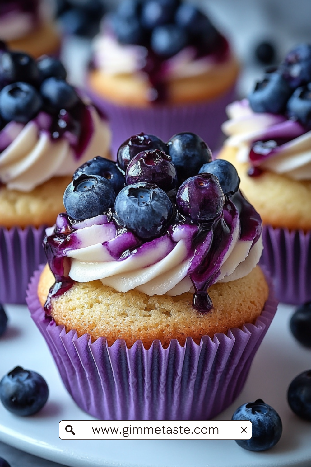 Close-up of White Chocolate Blueberry Cheesecake Cupcakes with swirled cream cheese frosting, blueberry jam drizzle, and fresh blueberries on top.