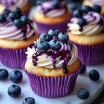 Close-up of White Chocolate Blueberry Cheesecake Cupcakes with swirled cream cheese frosting, blueberry jam drizzle, and fresh blueberries on top.