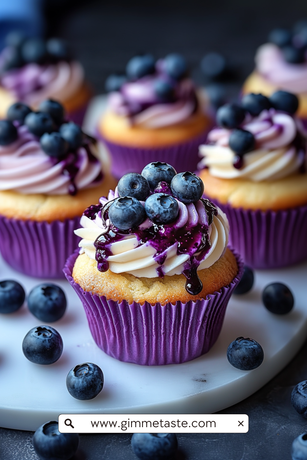 Close-up of White Chocolate Blueberry Cheesecake Cupcakes with swirled cream cheese frosting, blueberry jam drizzle, and fresh blueberries on top.