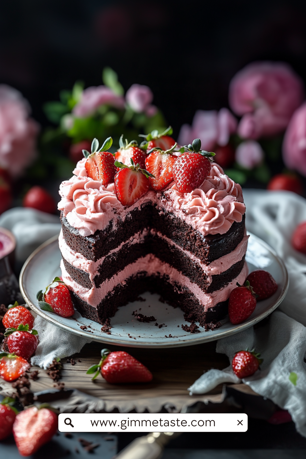 A decadent chocolate layer cake filled and topped with pink strawberry frosting, adorned with whole and halved fresh strawberries and edible flowers.