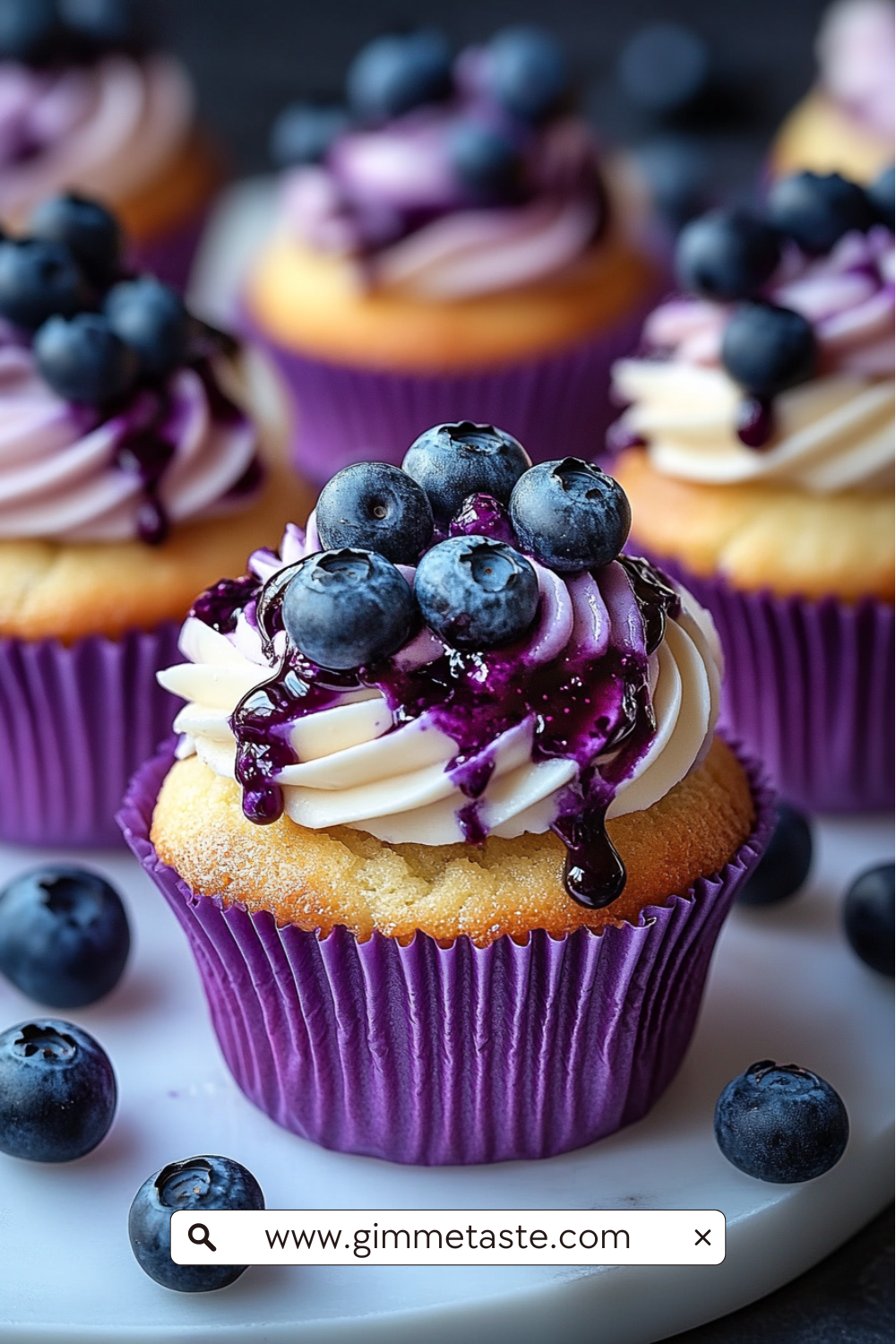 Close-up of White Chocolate Blueberry Cheesecake Cupcakes with swirled cream cheese frosting, blueberry jam drizzle, and fresh blueberries on top.